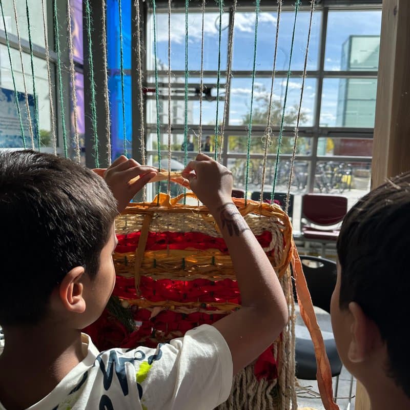 Community members weaving at the 6-foot cedar Earth Loom